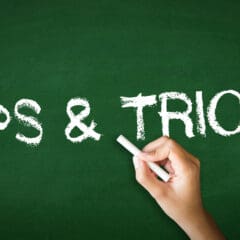 A hand holding a piece of chalk writes "TIPS & TRICKS" on a green chalkboard in white capital letters. The background is entirely green, resembling a school chalkboard.