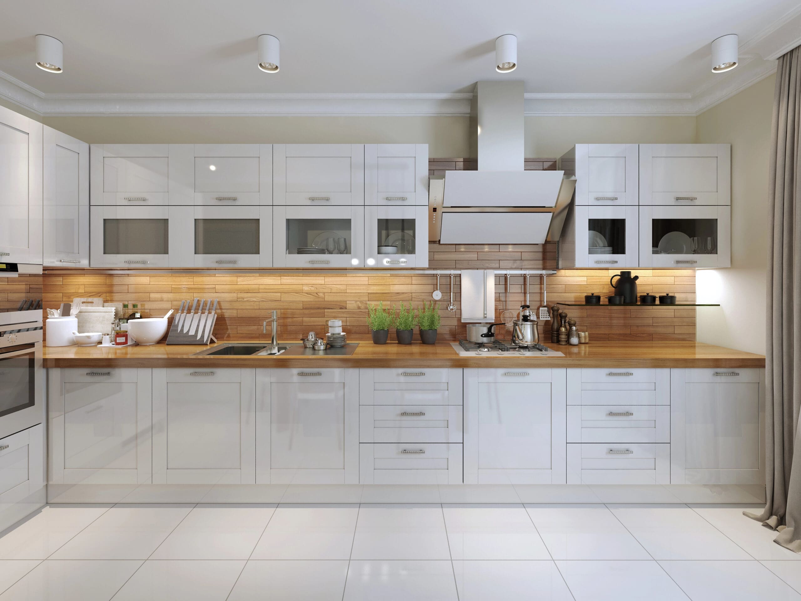 A modern kitchen with white cabinetry, a wooden countertop, and a glossy tile backsplash. The kitchen features a stainless steel range hood, an induction cooktop, and various kitchen utensils and appliances, including a kettle and a coffee maker, neatly arranged.